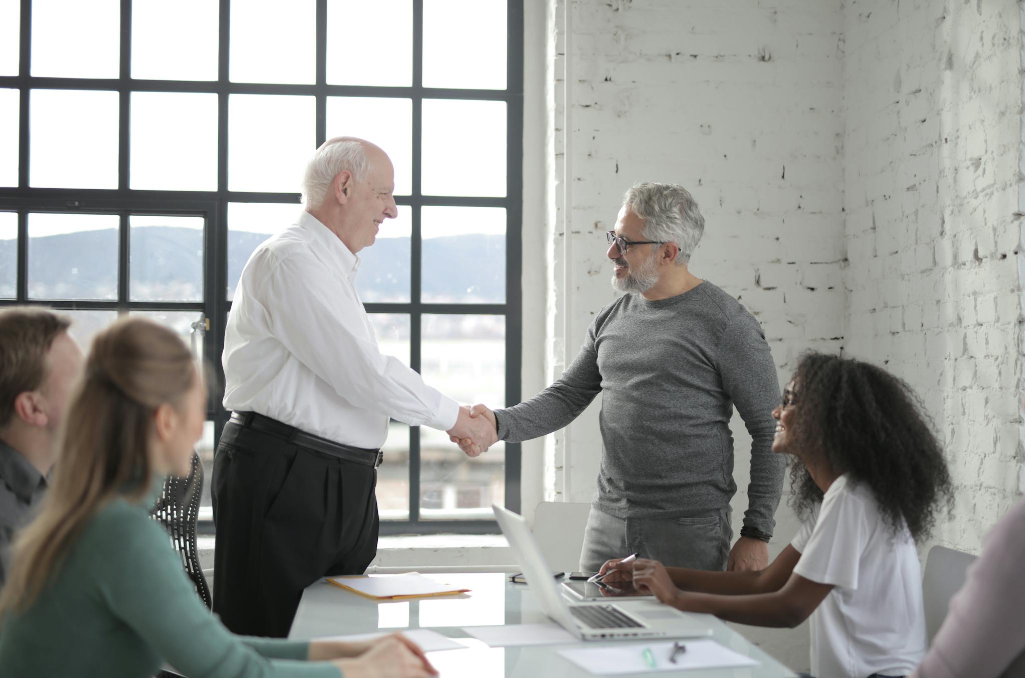 Group of diverse coworkers in office man middle aged and man senior shacking hands while working on project with colleagues